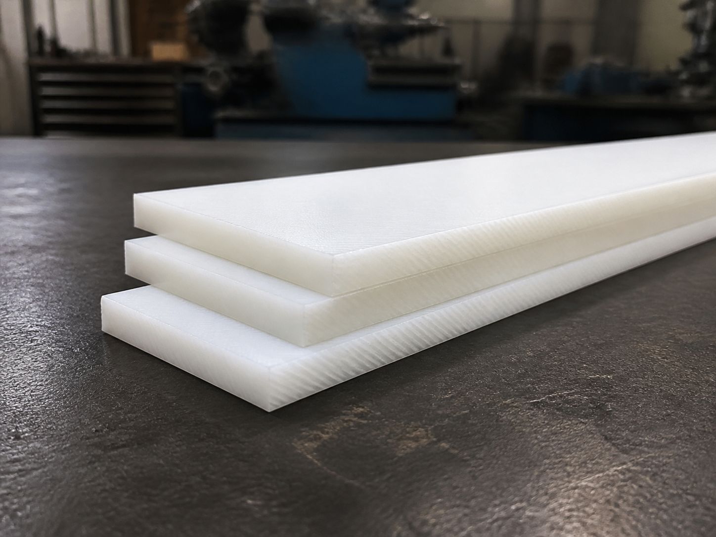 Three thick white polyethylene blanks stacked and fanned on a steel bench.