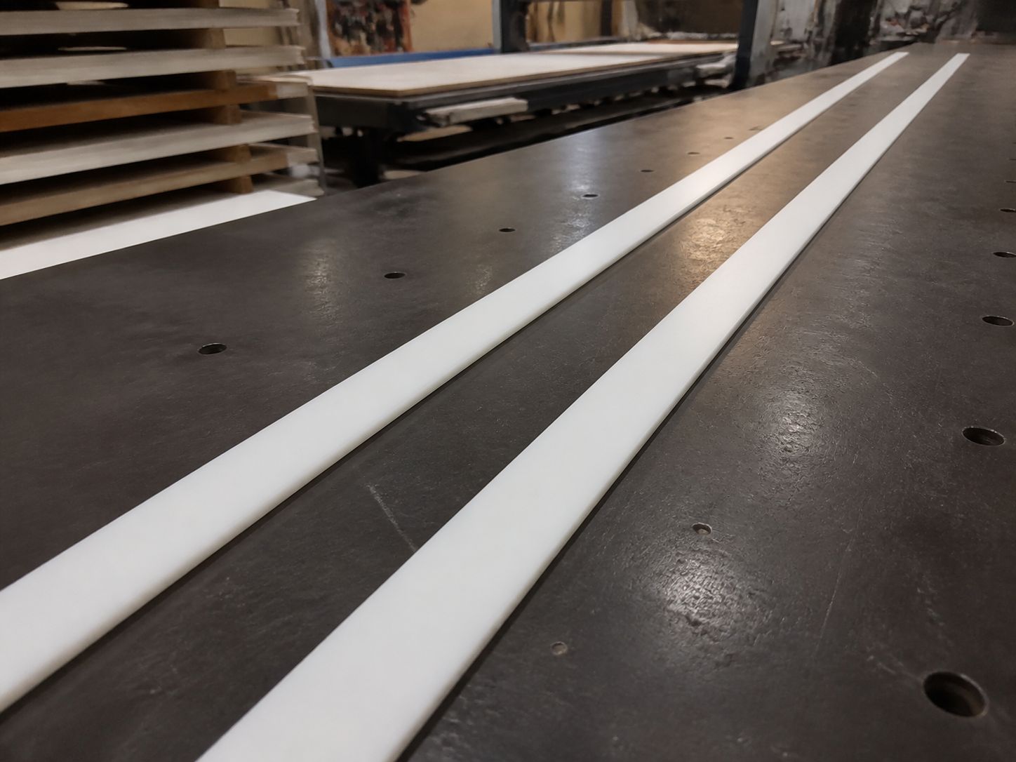 Three long slim white rails laid out on a bench with racks of sheet stock behind.