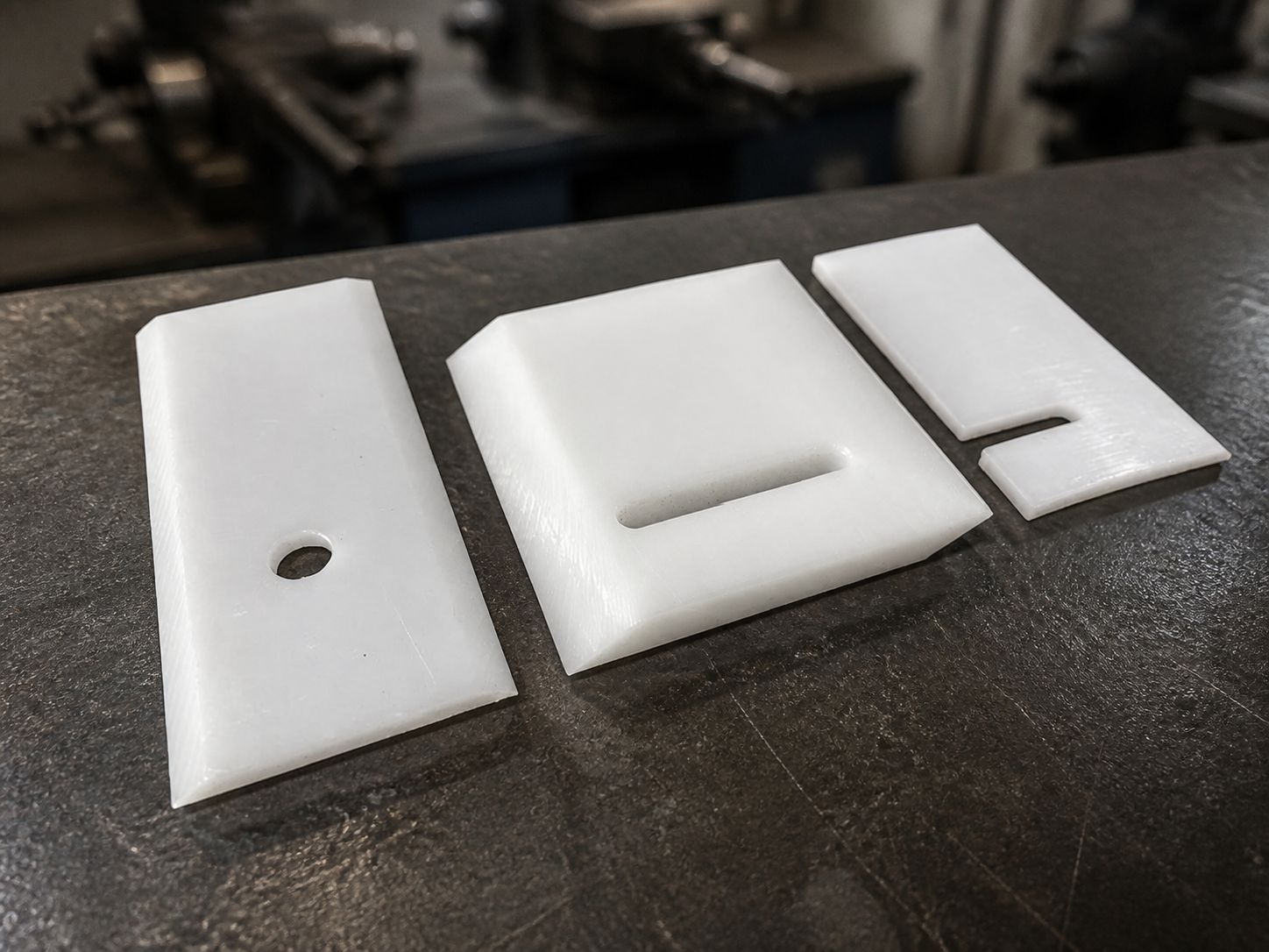 Three small white blades on a bench showing a round hole, a slotted cut-out and a corner notch.