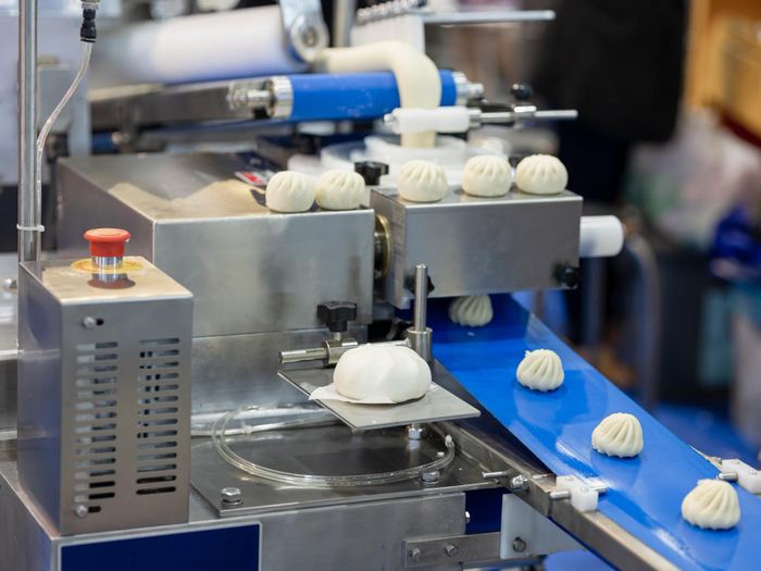 Stainless food production line moving dough portions along a blue conveyor belt.