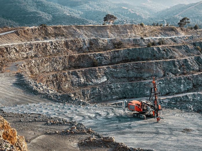 Benched walls of an open-pit mine with a drill rig working the floor.